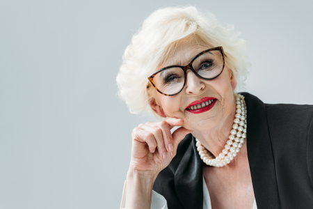 attractive senior lady with pearl necklace and eyeglasses, isolated on greyの写真素材