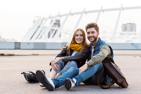 stylish couple looking at camera while resting on ground togetherの写真素材