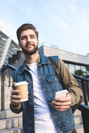 selective focus of smiling man with smartphone and coffee to go in hands on streetの写真素材