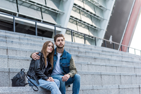 portrait of thoughtful couple looking away while sitting on stairs on streetの写真素材