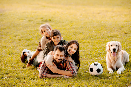 Happy family with two children lying in a pile on grass with dog sitting beside themの写真素材