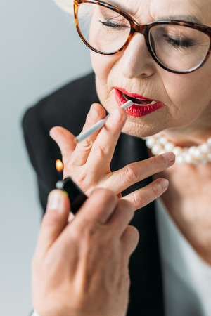 cropped view of senior lady with pearl necklace smoking cigarette, isolated on greyの写真素材
