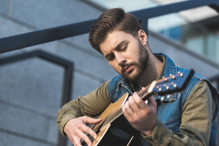 portrait of concentrated man playing acoustic guitar on street の写真素材