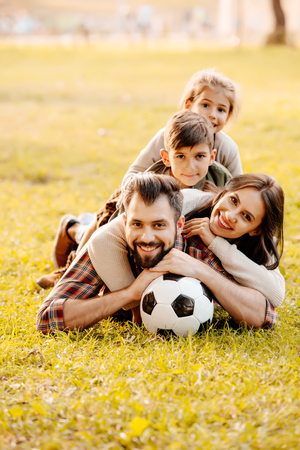 Happy family with two children lying in a pile on grass in a park