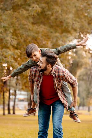 Father giving his little son a piggyback ride in autumn parkの写真素材