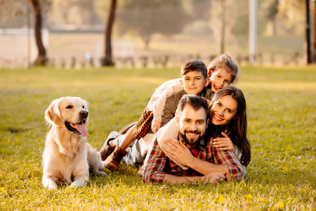 Happy family with two children lying in a pile on grass with dog sitting beside themの写真素材