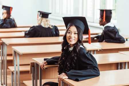 asian student girl in graduation costume sitting in class with multiethnic classmatesの写真素材