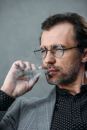 confident middle aged businessman in eyeglasses smoking cigarの写真素材