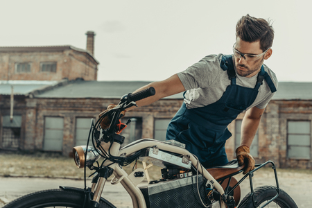 mechanic in goggles repairing vintage motorcycle standing outside at garageの写真素材