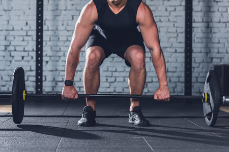partial view of man in sportswear lifting barbell in gymの写真素材