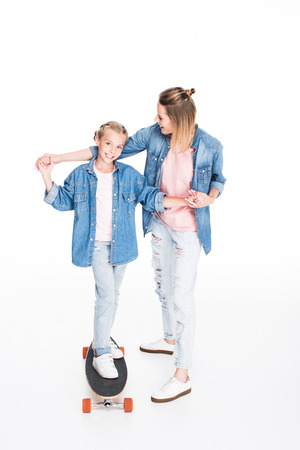 Mother helping little daughter to balance on longboard, isolated on whiteの写真素材