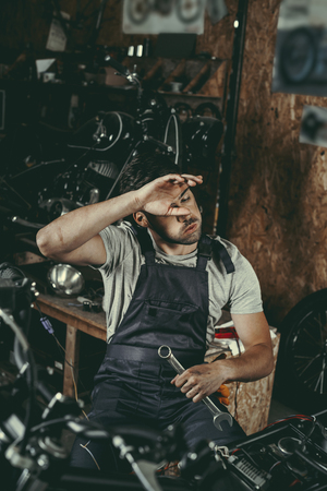 tired handsome mechanic repairing motorbike in workshopの写真素材