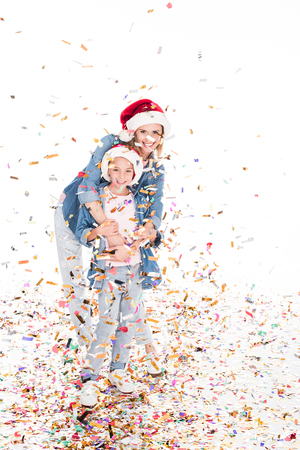smiling mother and daughter in Santa hats with confetti on christmas, isolated on whiteの写真素材