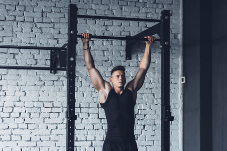 young man in sportswear doing pull ups on pull up bar in gym