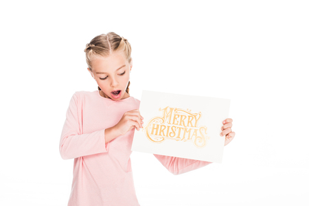 shocked child showing a card with text Merry Christmas, isolated on whiteの写真素材