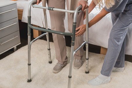 cropped shot of nurse helping senior patient with walker 