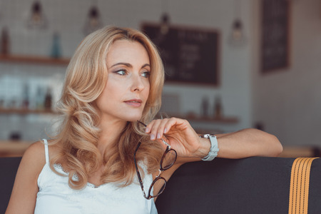 beautiful pensive middle aged woman holding eyeglasses and looking away の写真素材