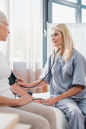 smiling nurse measuring blood pressure to senior patientの写真素材