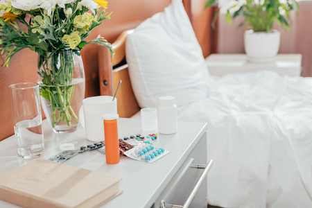 close-up view of pills with glass of water and empty hospital bed behindの写真素材