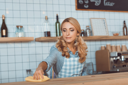 beautiful middle aged waitress in apron cleaning bar counter with ragの写真素材
