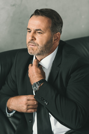 serious mature businessman in suit tying necktieの写真素材