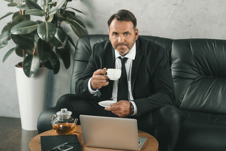 mature businessman drinking tea with laptop on table
