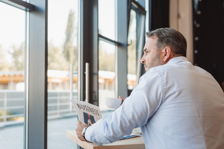 mature businessman with newspaper in cafe looking through windowの写真素材