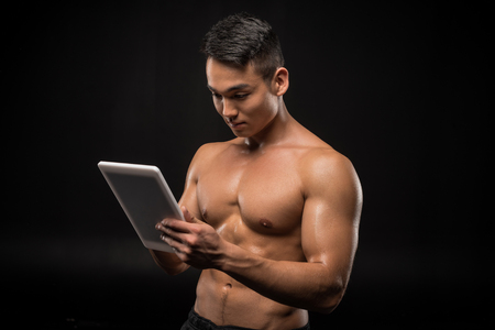 muscular shirtless man using digital tablet isolated on blackの写真素材