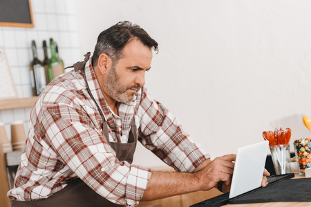 mature happy bartender using tablet at cafeの写真素材