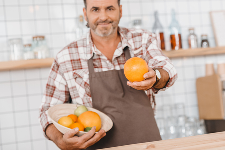 happy mature bartender with fruits in bowl looking at cameraの写真素材