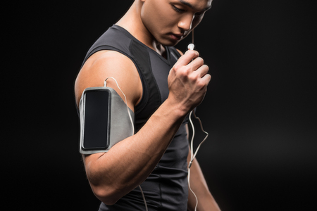 cropped shot of young asian sportsman listening music with smartphone and earphones の写真素材