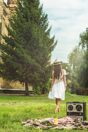 back view of stylish girl in straw hat walking on grass at parkの写真素材