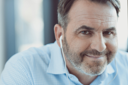 close-up portrait of smiling handsome mature man listening music with earphonesの写真素材