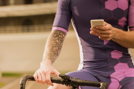 cropped shot of man in sportswear sitting on bicycle and using smartphoneの写真素材