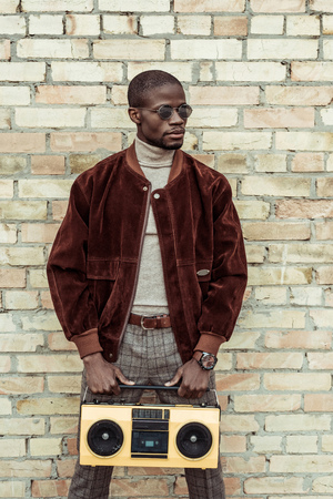 Handsome african american man in stylish clothes and sunglasses, holding a boombox