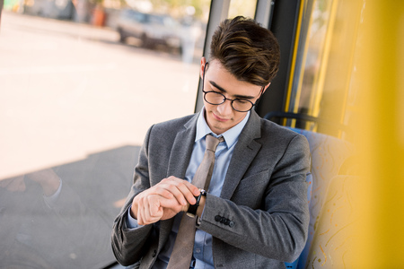 handsome young businessman in eyeglasses checking wristwatch while sitting in city busの写真素材