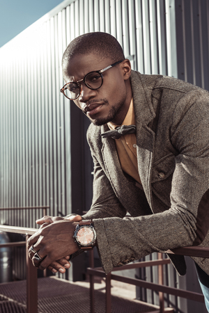 Stylish african american man in formal suit and glasses, leaning on guardrails and looking at cameraの写真素材