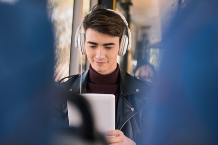 smiling young man in headphones using digital tablet in bus