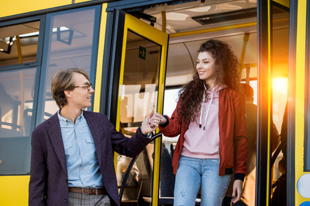 smiling young man in eyeglasses holding hand of happy girl in public transportの写真素材