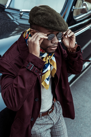 Young african american man posing in front of car and adjusting sunglasses on his faceの写真素材