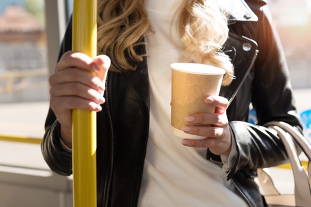 partial view of woman with coffee to go holding bus handleの写真素材