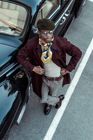 Stylish african american man posing in front of a car with hands on waistの写真素材