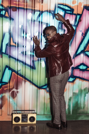 Handsome african american man in stylish clothes, painting graffiti on wall