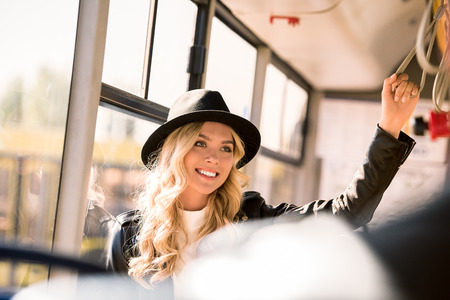 beautiful smiling young woman in hat standing and looking away in city busの写真素材