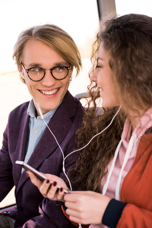 happy young couple in earphones listening music together with smartphone in busの写真素材