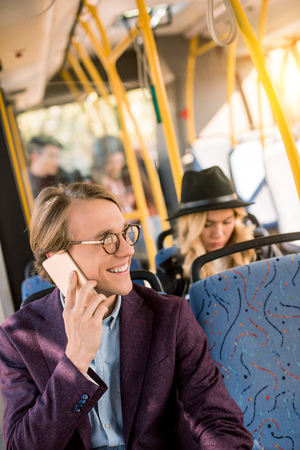smiling young man in eyeglasses taling on smartphone in busの写真素材