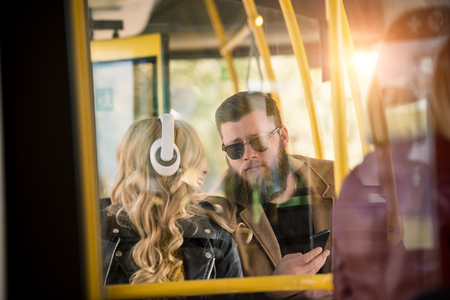 stylish young couple using smartphone and looking at each other in busの写真素材