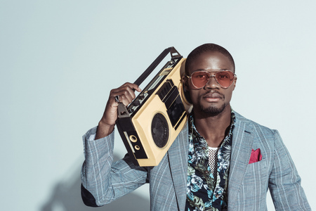 Young african american man in suit and sunglasses, holding a boombox and looking at camera
