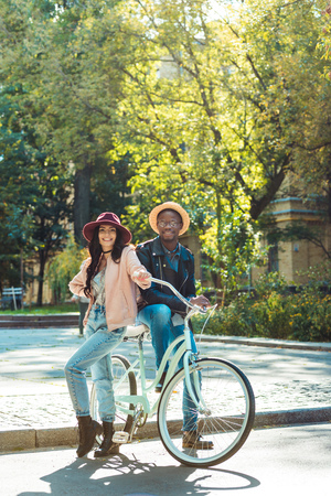 Beautiful multicultural couple standing together with a bicycle and posing to the camera の写真素材