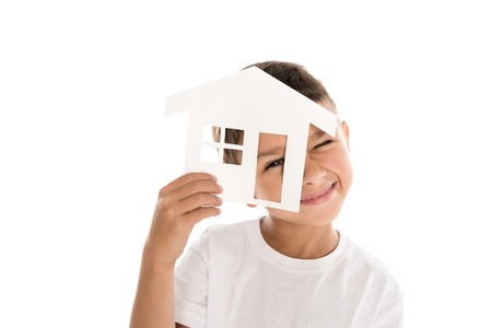 portrait of smiling boy looking at camera through house model isolated on white の写真素材
